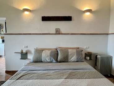 Se trata de un dormitorio acogedor que cuenta con una cama perfectamente hecha con ropa de cama a rayas, lámparas de pared, mesitas de noche suspendidas, una decoración minimalista y colores suaves que crean un ambiente relajante.