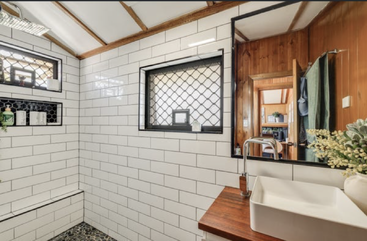 Cette salle de bains est dotée de carreaux de métro blancs, d'un plan de travail en bois surmonté d'un lavabo carré moderne, d'un grand miroir, d'encadrements de fenêtre noirs, d'étagères intégrées dans la douche et de plantes vertes.