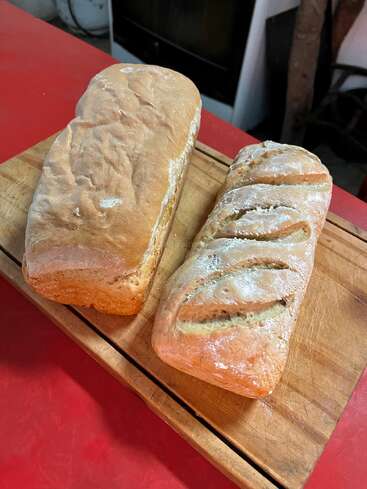 Zwei frisch gebackene Brotlaibe liegen auf einem hölzernen Schneidebrett. Ein Laib ist glatt, der andere hat dekorative Schlitze auf der Kruste.