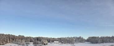 Un paysage hivernal serein composé d'arbres enneigés, d'une petite maison et d'une grange sous un vaste ciel bleu, évoquant la paix et le calme de la nature.