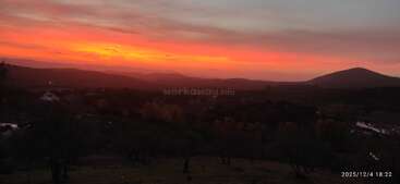 Un coucher de soleil époustouflant projette des teintes orange et rose vibrantes sur des collines ondulantes et un paysage sombre et paisible. Des silhouettes d'arbres et des montagnes lointaines complètent cette scène paisible.