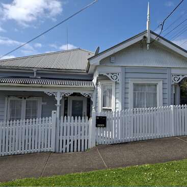 The image depicts a charming white house with a picket fence, featuring a grey roof and a small front porch, set against a serene blue sky with clouds.