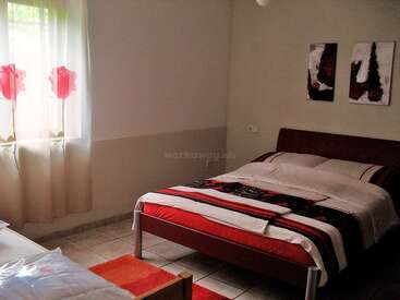 Das gemütliche Schlafzimmer verfügt über ein Doppelbett mit gestreifter Bettwäsche, moderne Gemälde, einen gefliesten Boden und ein Fenster mit geblümten Vorhängen. Das Licht erfüllt den Raum und schafft Wärme.