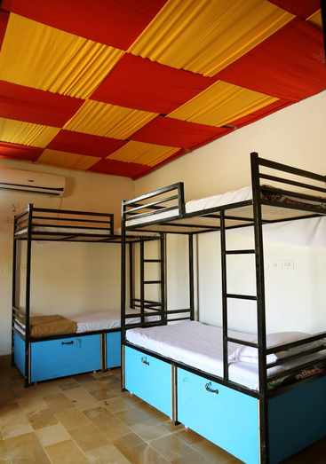 The image depicts a room with two bunk beds, each featuring black metal frames and white mattresses, situated on a tiled floor with a red and yellow checkered ceiling.