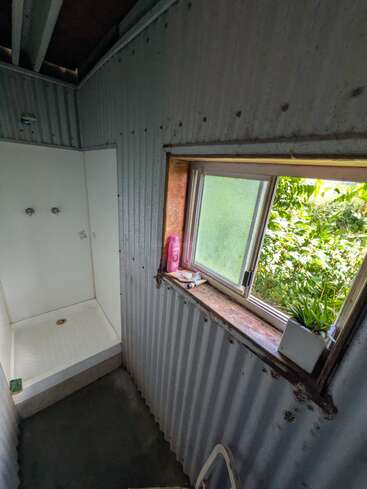 Cette photo montre une salle de bains au style rustique, avec des murs en tôle ondulée, une cabine de douche, une fenêtre donnant sur la verdure et une plante en pot posé sur le rebord de la fenêtre.