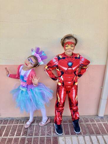Dos niños posan alegremente contra una pared. Uno va vestido de unicornio de colores con la cara pintada; el otro lleva un vibrante traje de Iron Man, también con la cara pintada.
