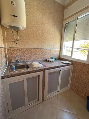 A small kitchen corner with a sink, granite countertop, and sliding cabinet doors. There are some plates, a sponge by the window, and a water heater above.