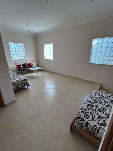 This room has tiled floors, cream walls, glass block windows, two couches with black-and-white covers, a metal coffee table, and colorful decorative cushions.