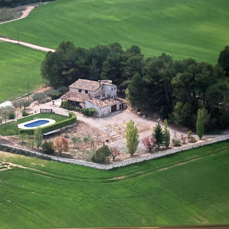 Das Bild zeigt eine Luftaufnahme eines großen Hauses mit Pool und Garten, das von Bäumen und Feldern umgeben ist und eine ruhige und malerische ländliche Landschaft darstellt.