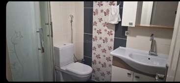 Dieses Badezimmer hat eine Glasdusche, eine weiße Toilette, Fliesen mit Blumenmuster, ein modernes Waschbecken mit Stauraum, einen Spiegelschrank und einen Handtuchhalter an der Wand.