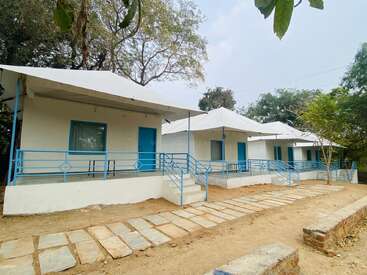 This image shows a row of white cottages with blue doors and railings, surrounded by trees. The ground is paved with stone slabs, creating a neat pathway.