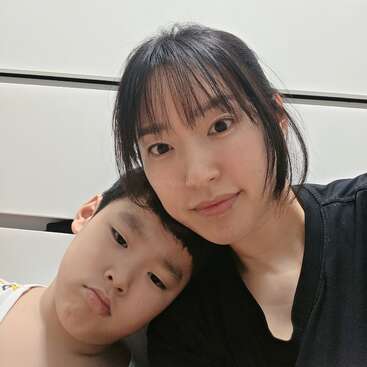 Une femme et un jeune garçon prennent un selfie en gros plan à l'intérieur. Le garçon pose sa tête sur l'épaule de la femme. Tous deux ont une expression neutre et regardent l'appareil photo.