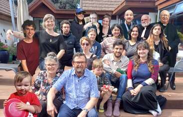 L'image représente un groupe de personnes diverses, adultes et enfants, rassemblées devant un bâtiment, posant pour une photo avec un sentiment d'unité et de camaraderie.