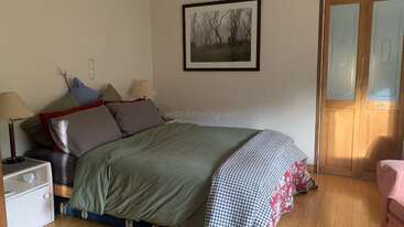 Esta acogedora habitación cuenta con una cama doble con ropa de cama verde, varias almohadas, dos lámparas de noche, un cuadro de la naturaleza enmarcado, suelo de madera y un armario.