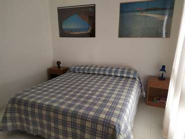 The image depicts a serene bedroom with a blue and white plaid bedspread, two nightstands, and two beach-themed pictures on the wall, creating a calming atmosphere.