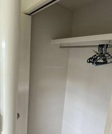 Das Bild zeigt einen leeren, weißen Schrank mit einer Kleiderstange und ein paar Kleiderbügeln aus Plastik. Der Schrank hat kahle Wände und keine Regale im Inneren.