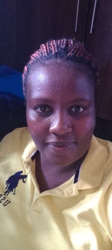 The image depicts a woman with dark skin and braided hair, wearing a yellow polo shirt with a black logo and text, set against a dark background.