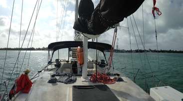 La imagen muestra un velero de casco blanco y gran vela, flotando en aguas tranquilas. El barco está situado en el centro del encuadre, con una visión clara del agua circundante.
