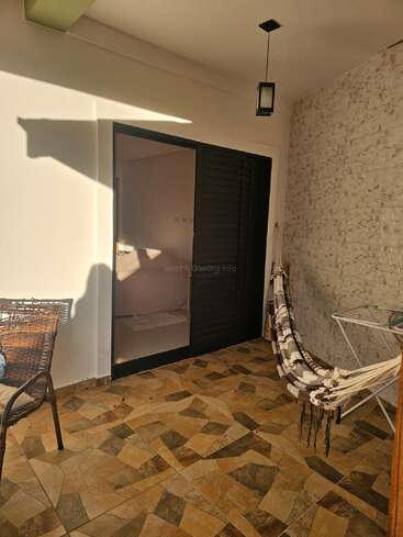 Este pátio aconchegante tem piso de azulejos estampados, cadeira de vime, rede listrada, lanterna suspensa, parede de pedra texturizada, porta de vidro deslizante e a luz do sol entrando com seu calor aconchegante.