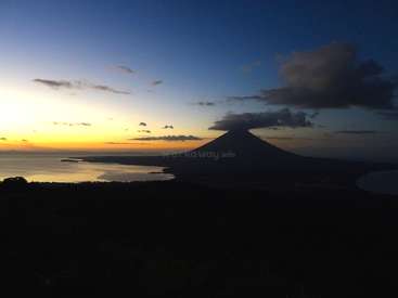 The image depicts a serene sunset scene featuring a majestic volcano, a tranquil lake, and a vibrant sky with clouds, set against a darkened foreground.