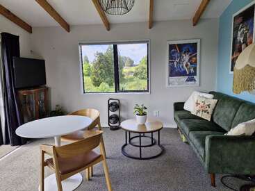Dieses gemütliche Wohnzimmer hat ein grünes Sofa, einen runden Tisch mit Holzstühlen, einen Fernseher, Star Wars-Poster, eine Zimmerpflanze, ein großes Fenster, freiliegende Balken und einen tollen Ausblick.