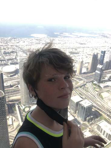 La imagen muestra a un chico joven con el pelo corto, vestido con una camiseta de tirantes negra, de pie delante de un paisaje urbano, posiblemente en un piso alto o en un balcón.