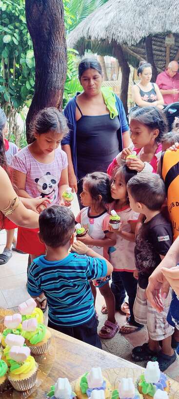 La imagen muestra a un grupo de niños reunidos en torno a una mesa, rodeados de un surtido de coloridas magdalenas y otras golosinas, probablemente celebrando una ocasión o acontecimiento especial.