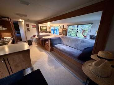 El acogedor interior de esta autocaravana cuenta con una pequeña cocina, un comedor y un largo sofá acolchado. Las ventanas aportan luz natural. La decoración incluye fotografías, sombreros y cuadros.