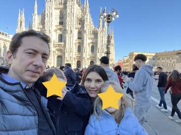 Una familia posa para una selfie frente a la catedral de Milán en un día soleado. Las caras de los niños están cubiertas con estrellas amarillas.