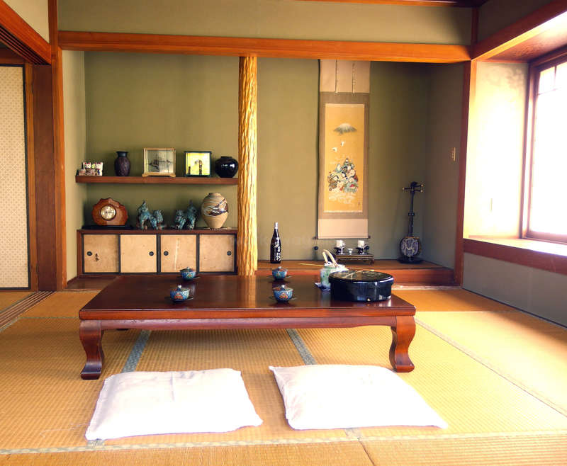 A imagem retrata uma sala serena em estilo japonês com uma mesa baixa de madeira, tapetes de tatame e decoração tradicional, exalando uma sensação de tranquilidade e herança cultural.