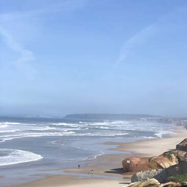 L'image représente une scène de plage sereine avec une vaste étendue de sable, de douces vagues et un ciel bleu clair, évoquant un sentiment de tranquillité et de relaxation.