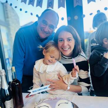 A joyful family celebrates a birthday together, smiling around a decorated cake. Bottles and festive decorations are on the table. The atmosphere is loving and cheerful.