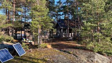 Una pequeña cabaña de madera enclavada entre altos pinos, con paneles solares en el suelo, luz solar a raudales y un apacible entorno de bosque natural que la rodea.