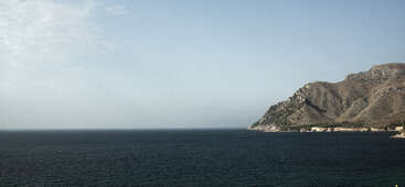 The image depicts a serene coastal scene, featuring a body of water with a shoreline and a mountainous area in the background, evoking a sense of tranquility and natural beauty.