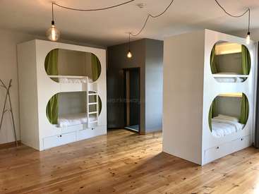 The image depicts a room with two bunk beds, each featuring a ladder and storage drawers, set against a backdrop of white walls and wooden floors.