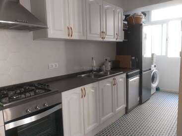 Il s'agit d'une cuisine moderne avec des armoires blanches, une cuisinière à gaz, un four, un double évier, un réfrigérateur, un lave-linge, de la lumière naturelle grâce à de grandes fenêtres et un sol à motifs.