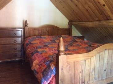 L'image représente une chambre à coucher confortable avec un cadre de lit et une commode en bois, un couvre-lit matelassé vibrant et un plafond en bois incliné.