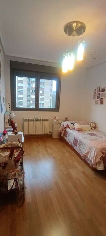 Esse quarto aconchegante tem piso de madeira, uma cama de solteiro com bichinhos de pelúcia, um carrinho de bebê, uma janela bem iluminada, luzes modernas e elementos decorativos simples na parede.