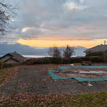 Un hermoso amanecer sobre unas montañas lejanas, con casas en primer plano. Las hojas caídas del otoño cubren el suelo y una piscina cerrada y cubierta de hojas. Una escena tranquila.