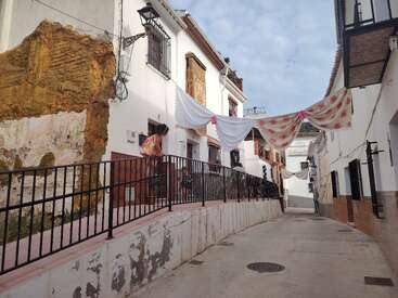 Eine schmale Straße in einem malerischen Dorf mit weiß getünchten Häusern, rustikalen Wänden, Wäscheleinen mit dekorativen Tüchern darüber und Metallgeländern schafft eine charmante, lebendige Atmosphäre.