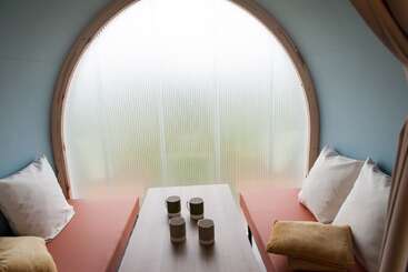 Ce pod confortable et moderne comprend deux banquettes avec des coussins blancs, une table en bois avec quatre tasses et une grande fenêtre circulaire dépolie laissant entrer une lumière douce.