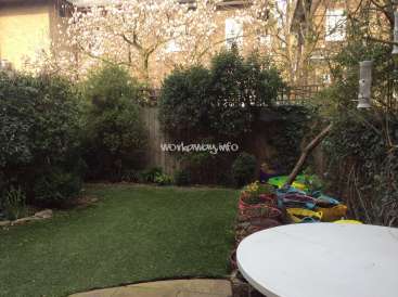 The image depicts a serene backyard scene, featuring a lush green lawn, a white table, and a wooden fence, with a subtle watermark reading "workaway.info".