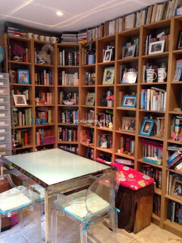 The image depicts a cozy room with a glass table and chairs, surrounded by a large bookshelf filled with books and decorative items.