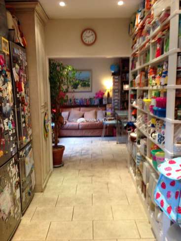 The image depicts a narrow hallway with a kitchen on the right and a living room on the left, featuring a clock, refrigerator, and shelves.