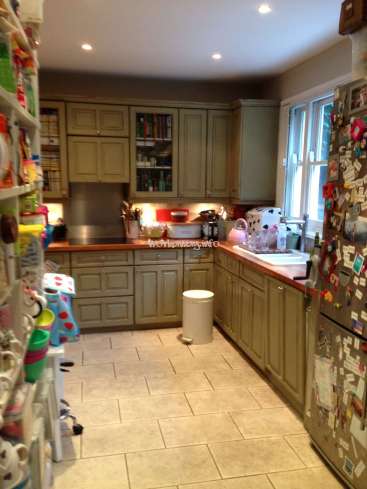 The image depicts a kitchen with beige cabinets and countertops, featuring a refrigerator, sink, and various appliances, with a window on the right side.