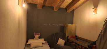 Une chambre chaleureuse et tamisée, avec des poutres apparentes au plafond, un lit simple, un fauteuil, un lit bébé rempli de balles, un oreiller en forme de chouette et des murs aux tons neutres. Une ambiance calme et accueillante.