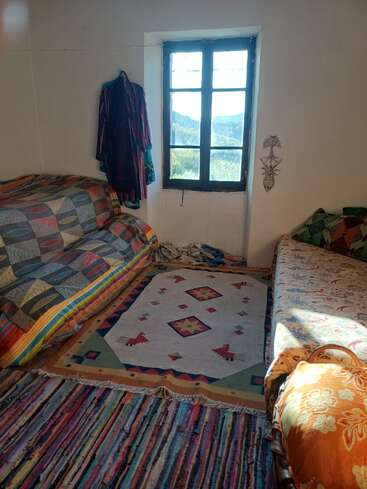 Una acogedora habitación con dos sofás de colores vivos, alfombras hechas a mano, una ventana con vistas panorámicas, ropa tendida, luz natural, cojines decorativos y un adorno de pared.