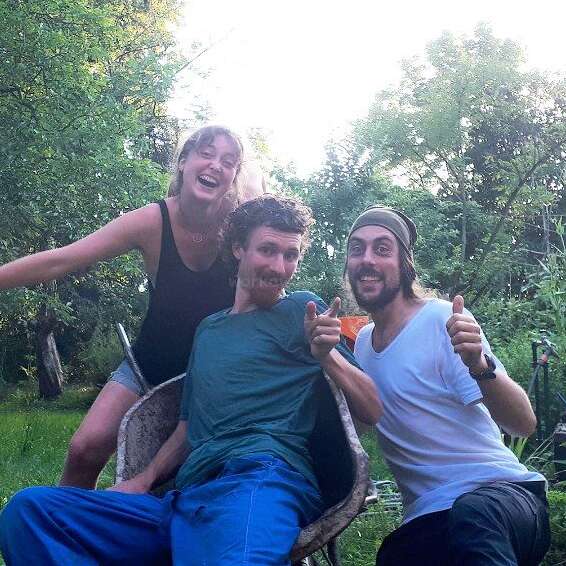 L'image représente trois personnes posant pour une photo dans un jardin luxuriant, entouré d'arbres et de plantes, transmettant un sentiment de joie et de camaraderie.