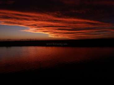 The image depicts a serene sunset over a body of water, with a darkened foreground and vibrant orange hues in the sky. The atmosphere is peaceful and calming.