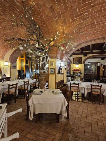Este acogedor restaurante presenta techos arqueados de ladrillo, muebles de madera, manteles blancos y un hermoso árbol decorativo adornado con luces y adornos, que crean un ambiente cálido.
